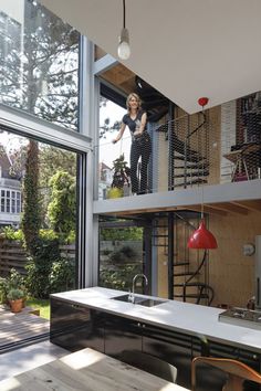 a woman standing on the balcony of a house with an open kitchen and dining area