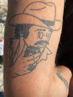 a close up of a person with a tattoo on his arm and the image of a man wearing a hat