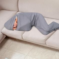 a man laying on top of a couch covered in a blanket next to a remote control