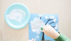 a young boy is making a paper tree with white flowers on it and a blue plate next to him