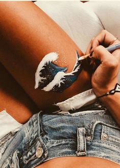 a woman with white paint on her stomach is painting the side of her thigh and holding a pen