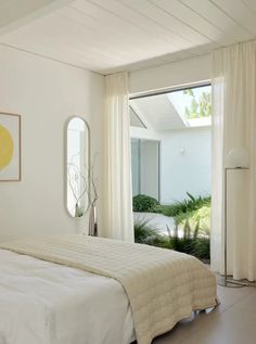 a bedroom with white walls and flooring has a large bed in front of the window