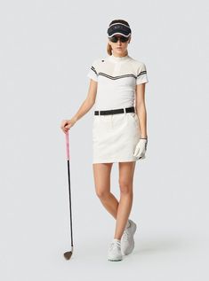 a woman is holding a golf club and wearing a white dress with black trims