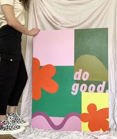 a woman standing next to a painting with the words do good on it