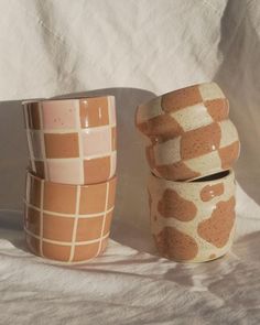 three cups are stacked on top of each other in different patterns and shapes, one is brown and the other is white