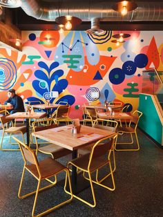 the interior of a restaurant with brightly painted murals on the wall and wooden tables in front of them