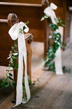 two wooden pews decorated with white ribbons and greenery