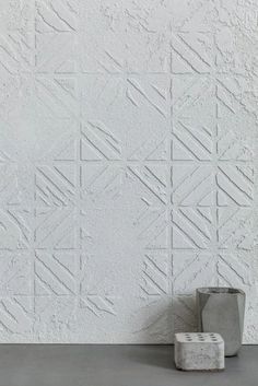 two vases sitting on the ground in front of a white wall with geometric designs