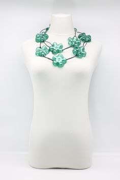 a white mannequin holding a green necklace on it's neck with flowers