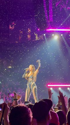 a woman standing on top of a stage with her arms in the air while singing