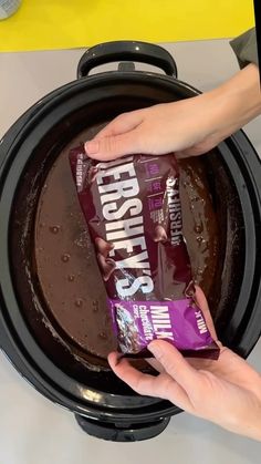 a person holding a bag of protein bar in front of a crock pot filled with chocolate