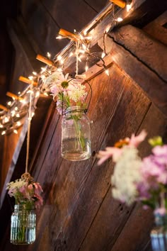 mason jars filled with flowers are hanging from a wooden beam in an outdoor area that is lit up by string lights