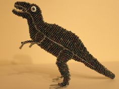 a toy dinosaur made out of beads on a white surface with an eyeball in it's mouth