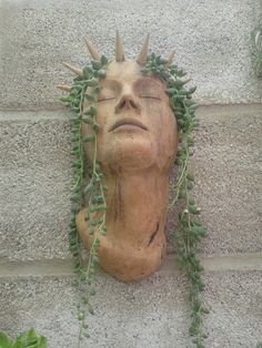 a statue with plants growing out of it's head on the side of a building