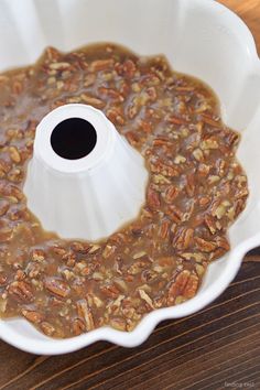 a white cake pan filled with pecans on top of a wooden table next to a knife