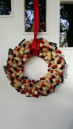 a wreath made out of wine corks hangs on the front door with red ribbon