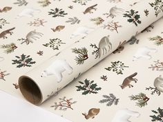 a white wrapping paper with animals and pine cones on it's side, next to a wallpaper roll