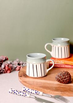 two coffee mugs sitting on top of a wooden cutting board next to some books