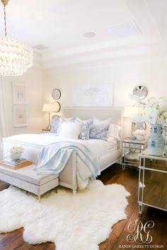 a white bedroom with a chandelier hanging from the ceiling and a large bed