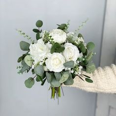 a bouquet of white roses and greenery in someone's hand