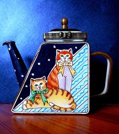 an orange and white cat sitting on top of a blue teapot next to a black coffee pot