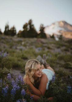 a woman laying on the ground with flowers in front of her and mountains in the background