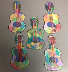 four colorful guitar shaped magnets sitting on top of a gray table next to each other