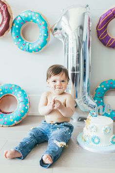 a baby sitting on the floor next to a cake and some doughnuts with sprinkles