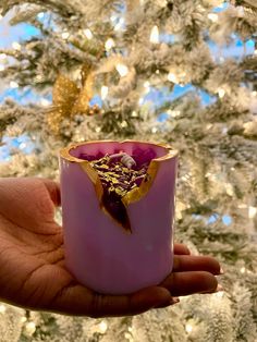 a hand holding a pink candle in front of a white christmas tree with gold decorations