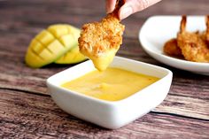 a person dipping something into a small bowl of yellow sauce on top of a wooden table