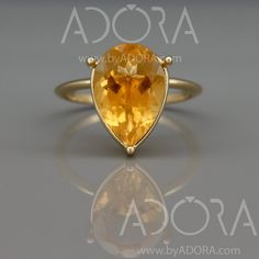 an oval shaped yellow topazte ring sits on a reflective surface in front of a gray background