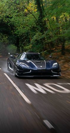 a black sports car driving down the road in front of trees and leaves on both sides