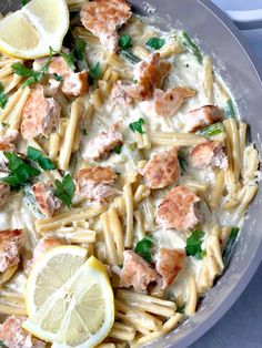 a skillet filled with pasta and meat covered in sauce next to lemon wedges