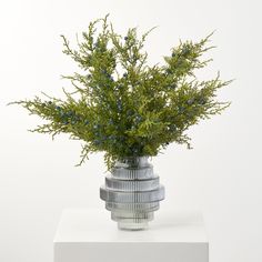 a silver vase with blue flowers in it sitting on a white table top next to a wall