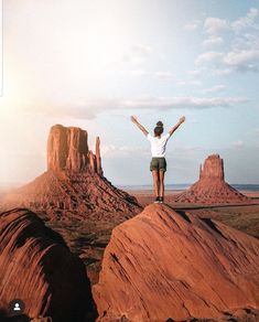 a woman standing on top of a rock formation with her arms outstretched in the air