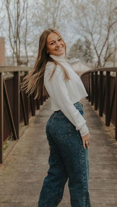 a woman standing on a sidewalk wearing high waist jeans and a white top with long sleeves