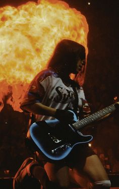 a person with a guitar in front of a fire ball