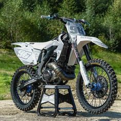 a white dirt bike parked on top of a metal stand in front of some trees