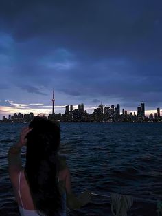 a woman sitting on top of a boat looking at the city skyline in the distance