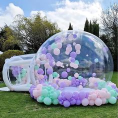 an inflatable bubble filled with pink and green balloons sitting on top of a lush green field