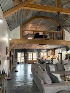 a living room filled with lots of furniture under a wooden beamed ceiling over a kitchen