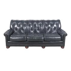 a black leather couch with wooden legs and buttons on the armrests, against a white background