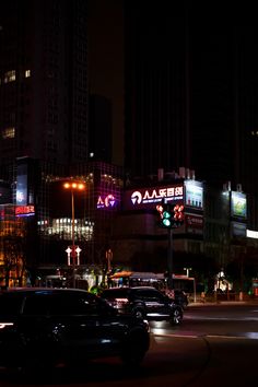 cars driving down the street at night in front of tall buildings with neon signs on them