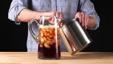 a man pours liquid into a pitcher filled with ice cubes on a wooden table