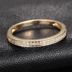 a gold wedding band with rows of diamonds on the inside and outside, sitting on a black leather surface