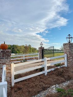 a white fence with a pumpkin sitting on top of it next to a brick wall