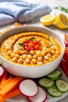 a white bowl filled with chickpeas and carrots next to sliced cucumbers