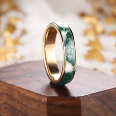 a wedding ring with green and white marble inlay on top of a wooden stand