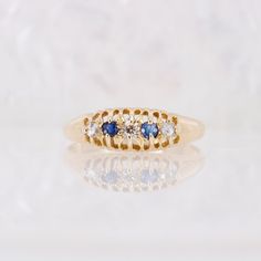 a yellow gold ring with three diamonds and blue sapphires on the side, sitting on a white surface