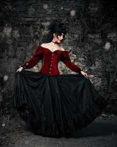 a woman in a red and black corset is standing by a stone wall